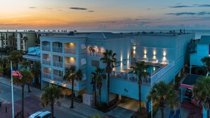 Un hotel con bar en la azotea, varios balcones y vistas al océano al atardecer.