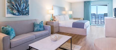 A modern hotel room with a sofa, a bed, a coffee table, and a balcony with a view.