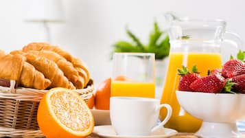 Een ontbijttafel met croissants, sinaasappelsap, aardbeien en een glas sinaasappelsap.