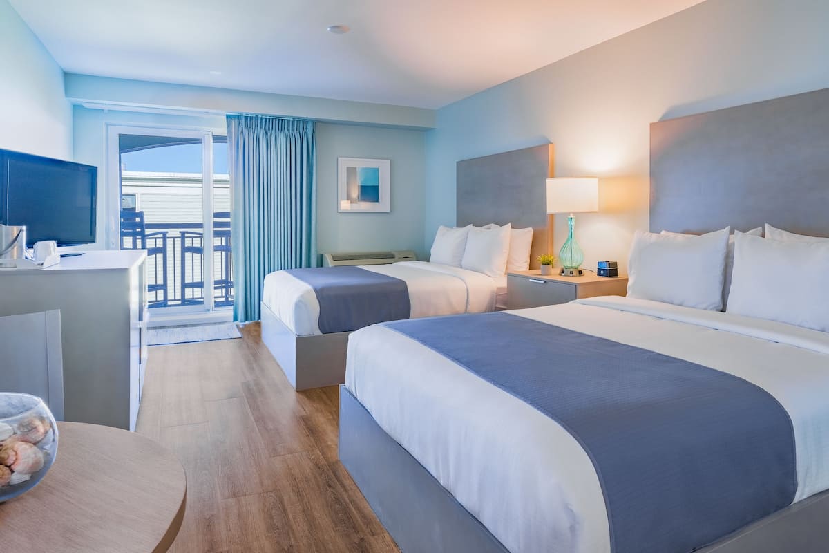 Habitación de hotel con dos camas, un escritorio, un televisor y un balcón con vistas.