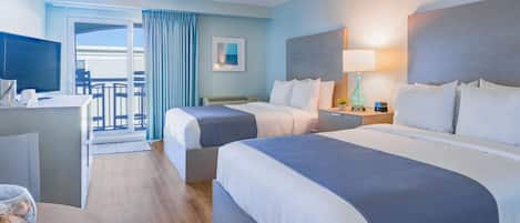 A hotel room with two beds, a desk, a television, and a balcony with a view.