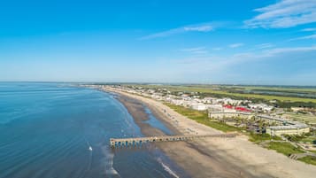 Vue aérienne d’une zone côtière comprenant une plage, une jetée et un quartier résidentiel avec des bâtiments.