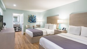 Habitación de hotel con dos camas, un escritorio, una silla, un televisor y un baño visible a través de una puerta abierta.