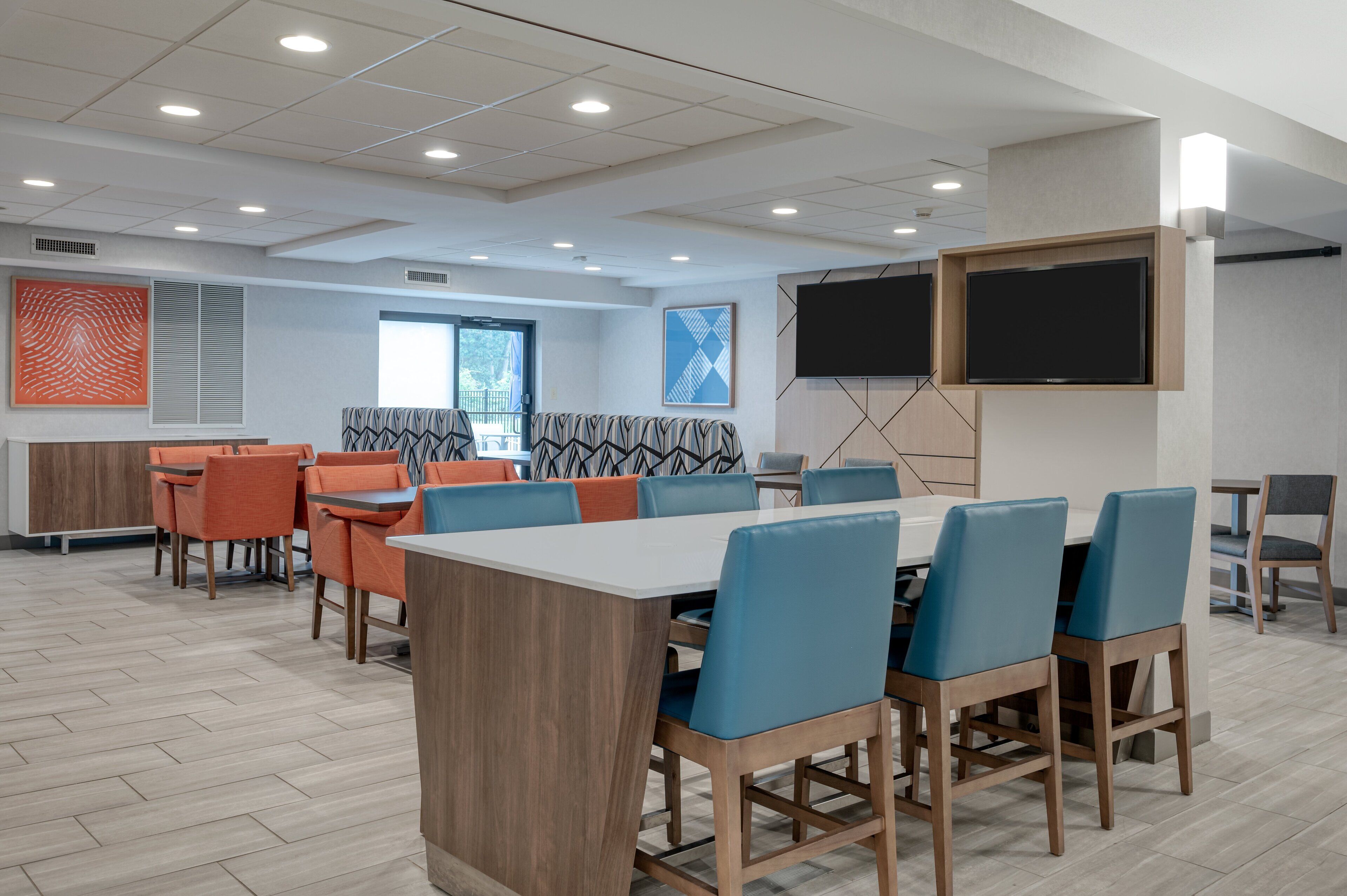 Un comedor moderno con mesas de madera y sillas azules, una pantalla grande y decoración mural con diseños.