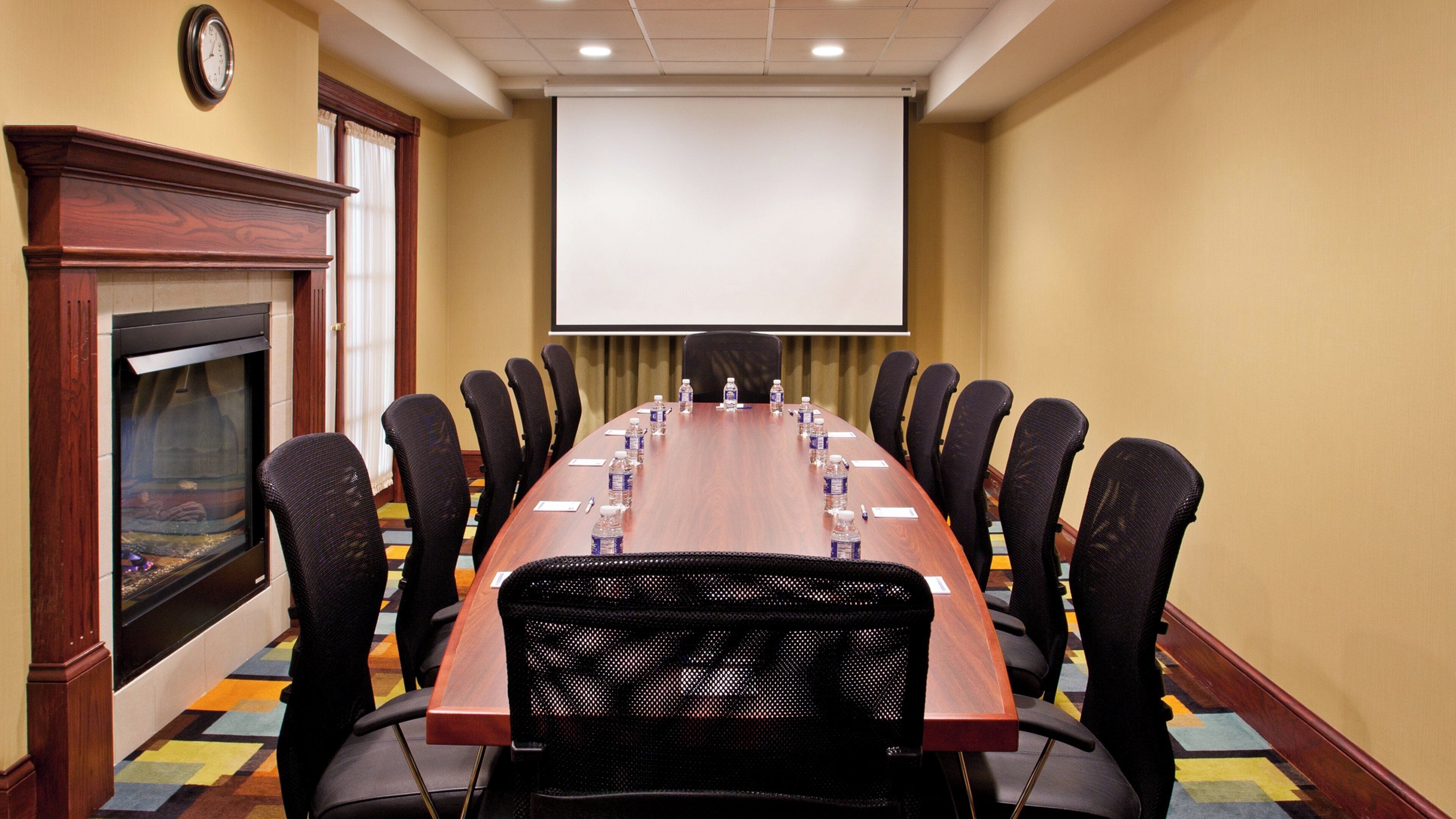 Une salle de conférence équipée d’une longue table, de chaises, d’un écran de projection et d’une cheminée.