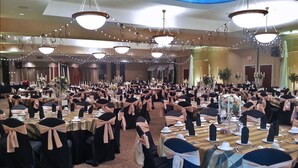 Une salle de banquet avec des tables rondes, des chaises noires et blanches, et des guirlandes lumineuses.