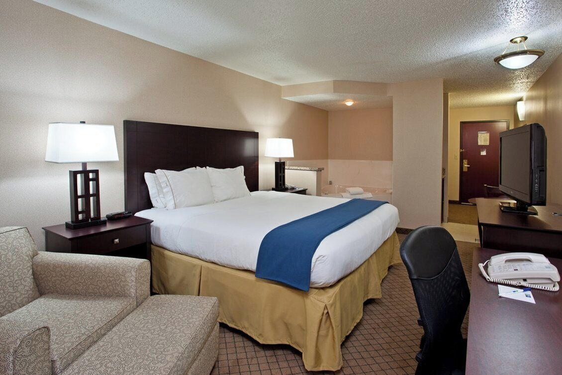 A hotel room with a bed, bedside tables, a desk, a chair, a television, and a telephone.