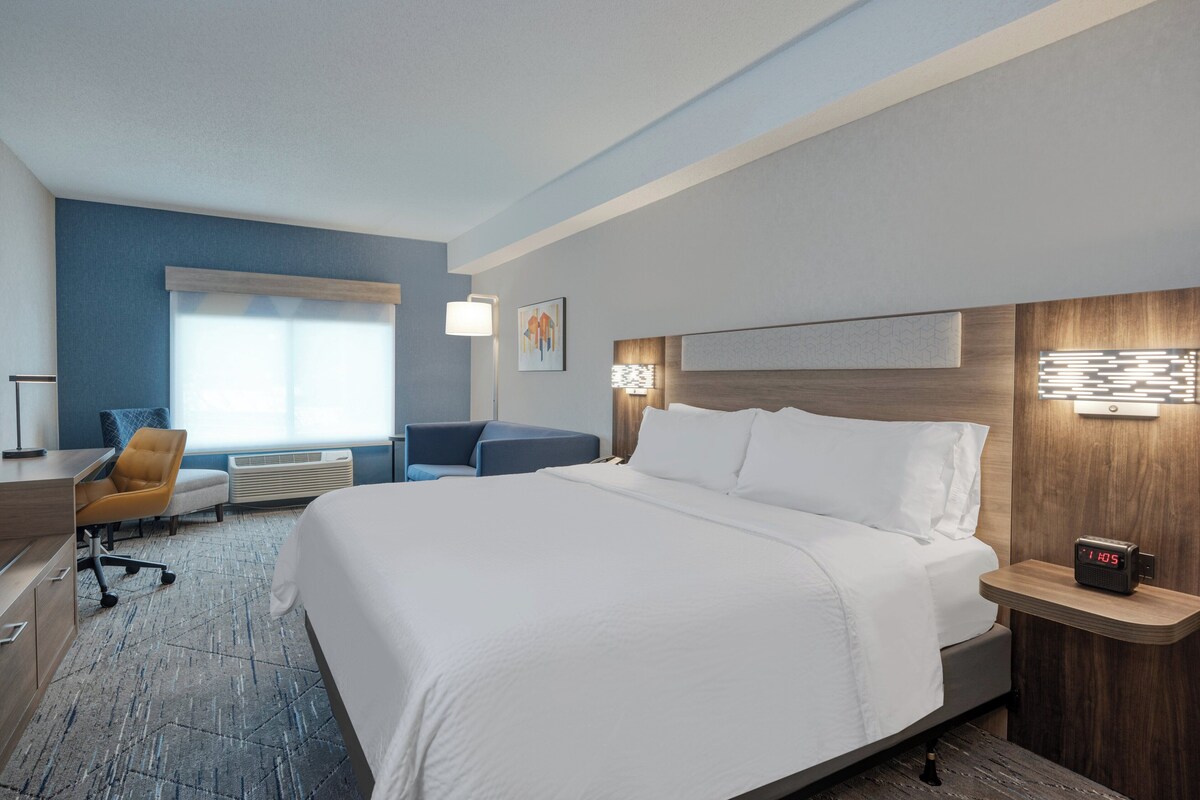 Een hotelkamer met een groot bed, een bureau, een stoel, een raam en een wandklok.