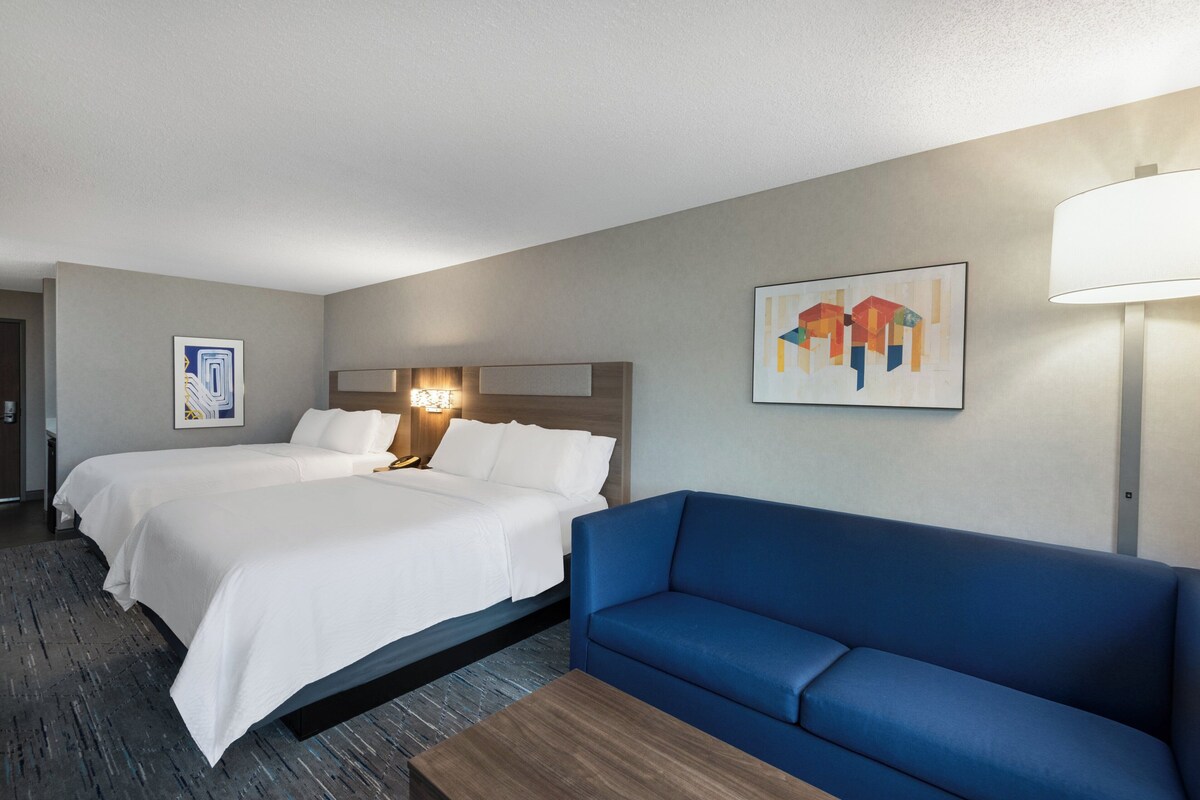 Een hotelkamer met twee bedden, een blauwe bank, een houten bijzettafeltje en kunstwerken aan de wanden.