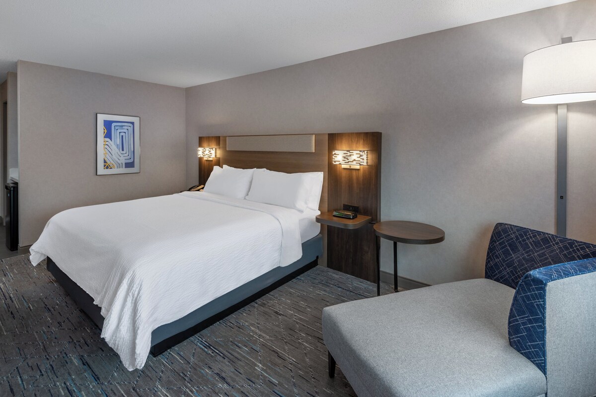 Een hotelkamer met een bed, nachtkastjes, een stoel en een wandlamp.