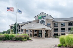 A Holiday Inn Express & Suites hotel with a brick facade, a covered entrance, and an American flag.