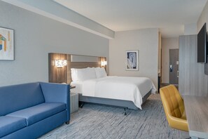 A hotel room with a bed, a blue sofa, a wooden desk, and a television.