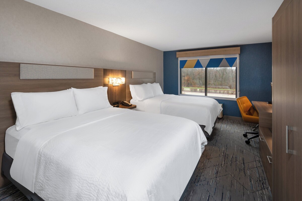 Een hotelkamer met twee bedden, een bureau, een stoel en een raam met uitzicht op bomen.