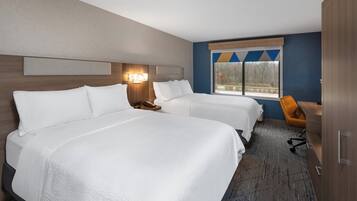 A hotel room with two beds, a desk, a chair, and a window with a view of trees.