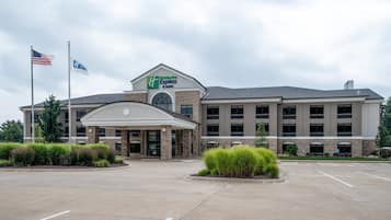 Um hotel Holiday Inn Express & Suites com fachada de tijolos, amplo estacionamento e bandeiras americanas.