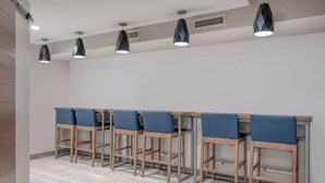 A row of bar stools with blue cushions, a wooden table, and pendant lights with geometric patterns. - Holiday Inn Express & Suites Wadsworth by IHG (Wadsworth)