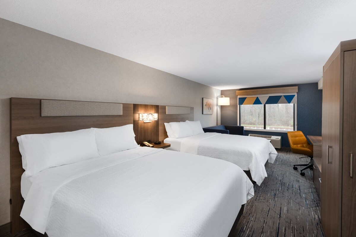 A hotel room with two beds, a desk, a chair, and a window with a view.