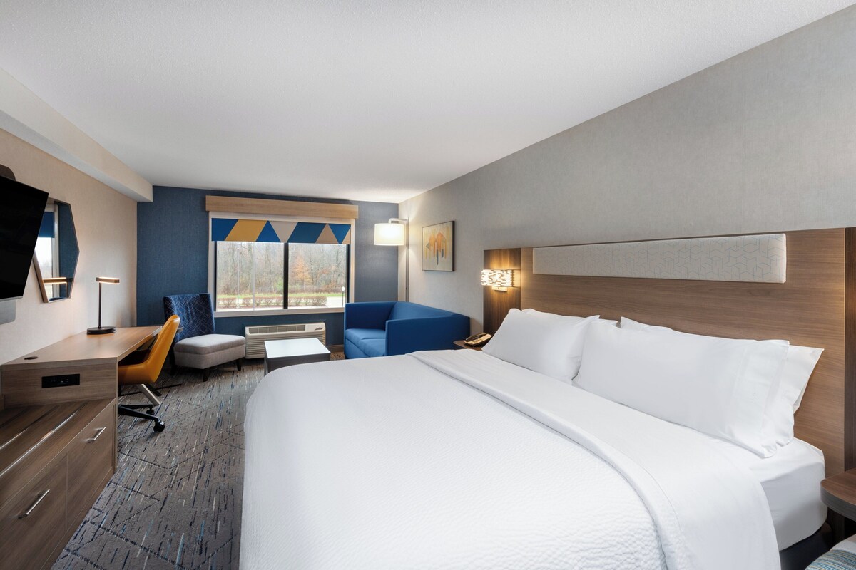Een hotelkamer met een groot bed, een bureau, een stoel, een bank en een raam met uitzicht.