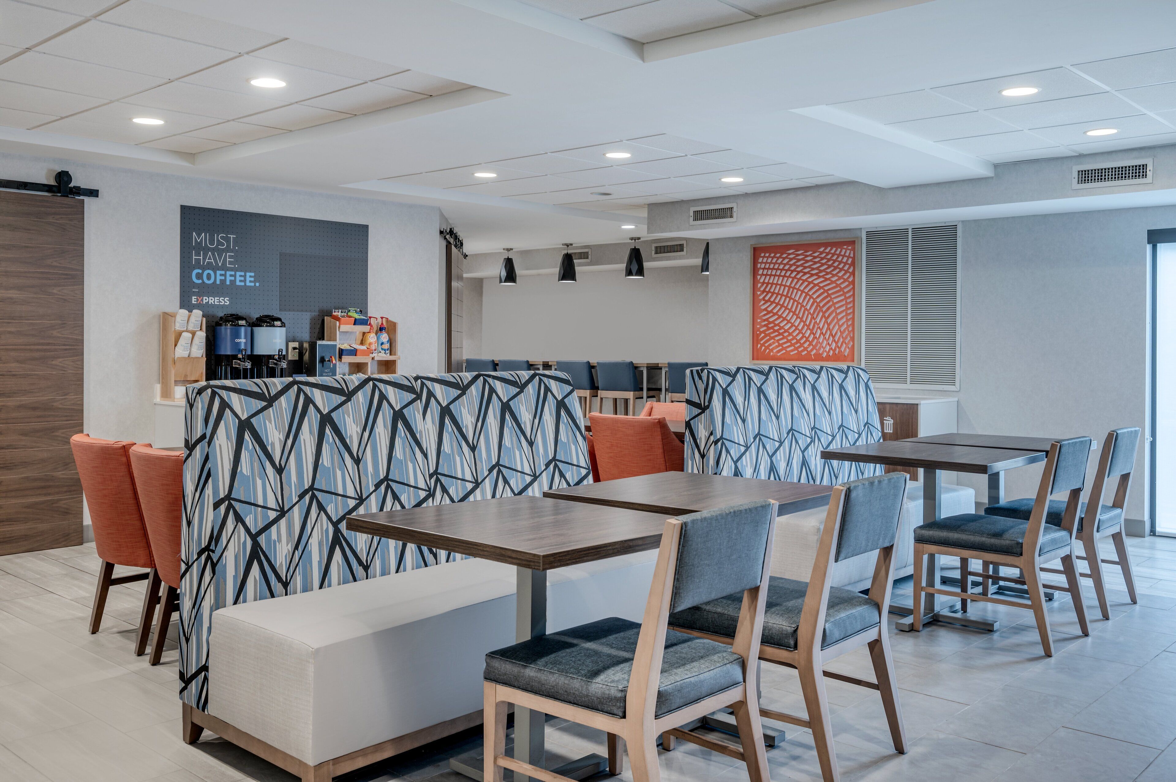 A modern cafe with seating arrangements, a coffee station, and a decorative wall.