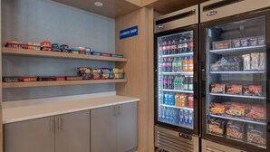 Un espace de restauration en libre-service, avec des étagères remplies de divers en-cas et un réfrigérateur-vitrine contenant des boissons et des aliments emballés.