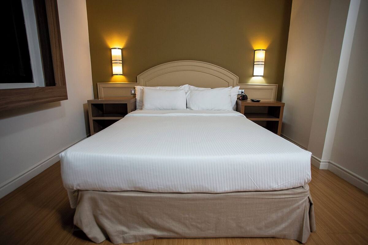 A neatly made bed with a headboard, two bedside tables, and wall-mounted lamps.