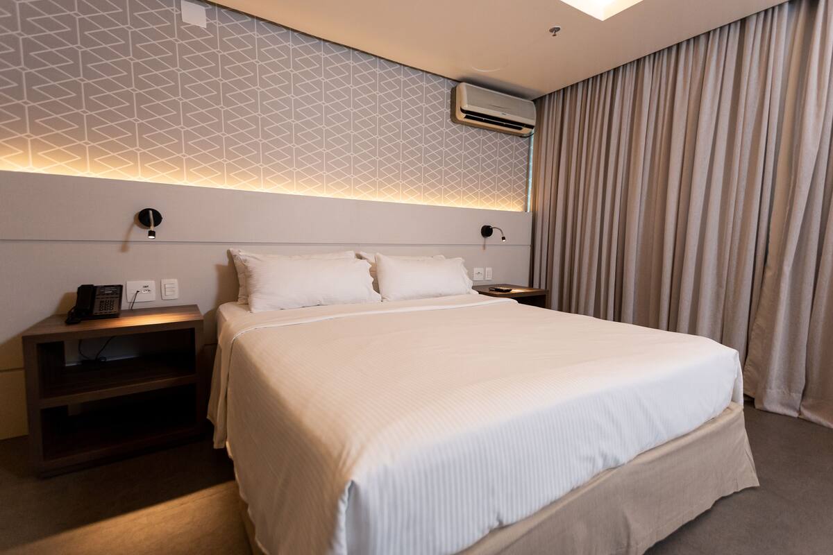 A modern hotel room with a large bed, a bedside table with a phone, and a wall-mounted air conditioner.