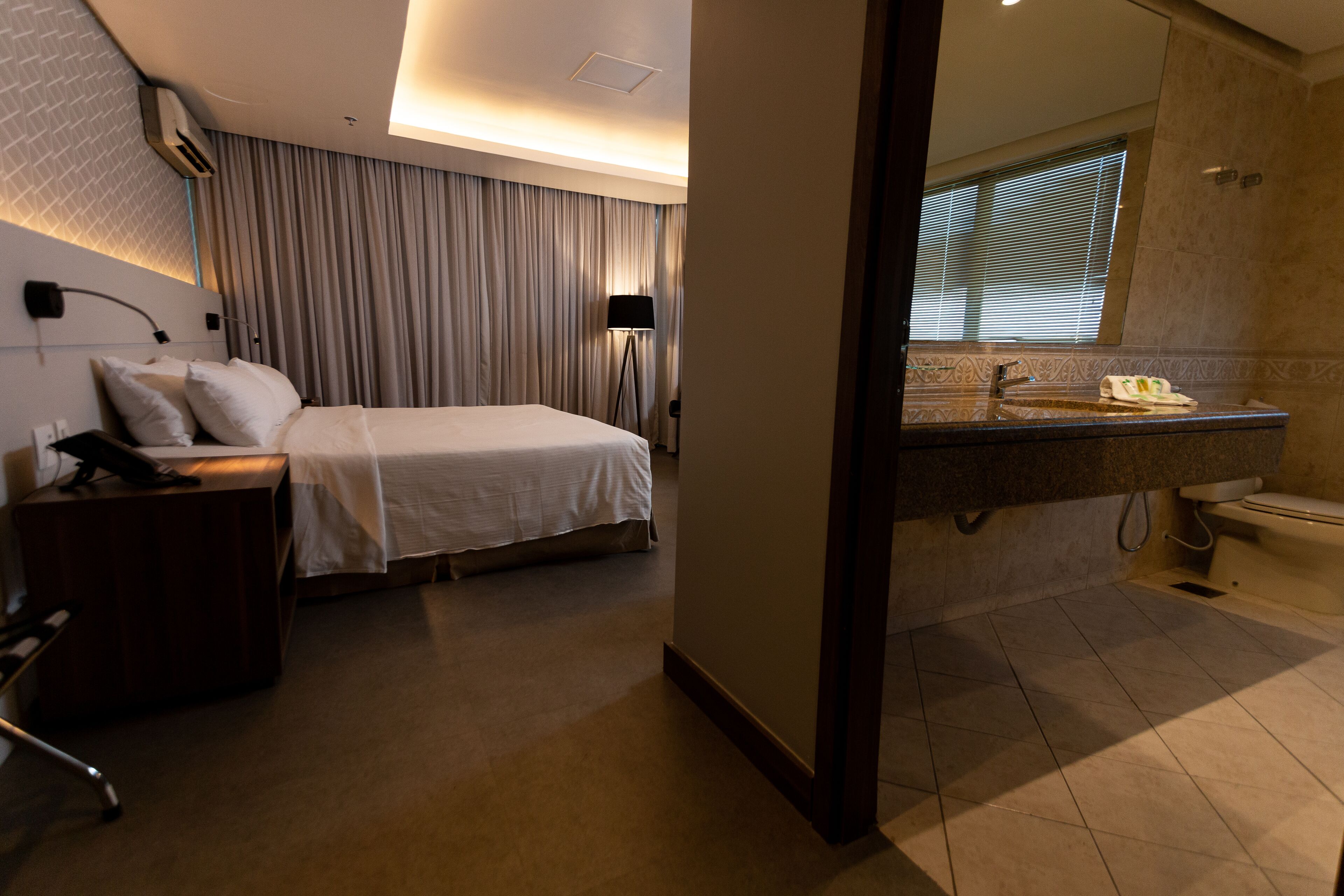 Une chambre d’hôtel comprenant un lit, une table de chevet, une lampe et une salle de bain avec un lavabo et des toilettes.