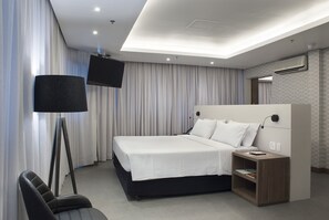 Moderni hotellihuone, jossa on suuri sänky, työpöytä lampun kanssa ja seinälle asennettu taulutelevisio.