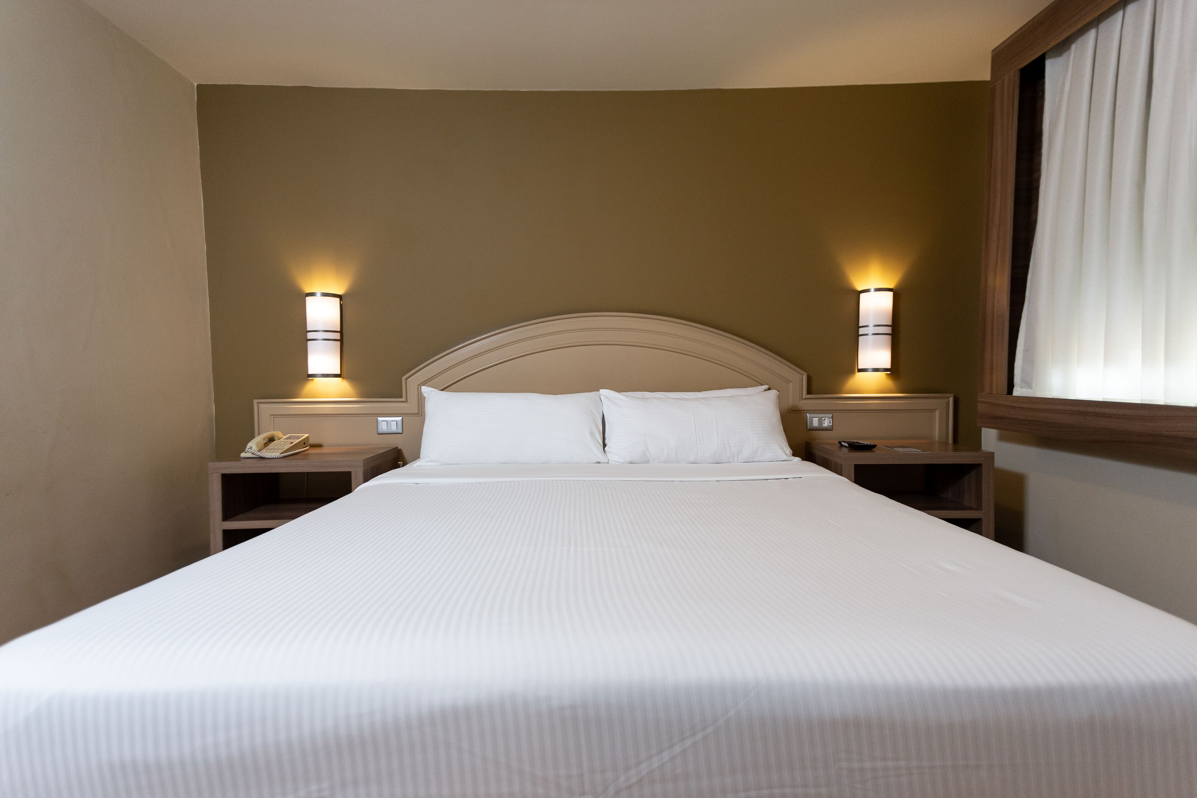 A neatly made bed with white linens, two bedside lamps, and a nightstand with a telephone.