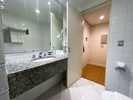A modern bathroom with a granite countertop, a large mirror, a toilet, and a shower area.