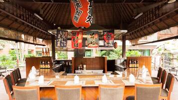 A restaurant with a long wooden counter, multiple seating areas, and hanging decorations.