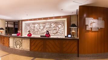 A reception desk with a large floral carving, two receptionists, and a sign for Holiday Inn Resort.