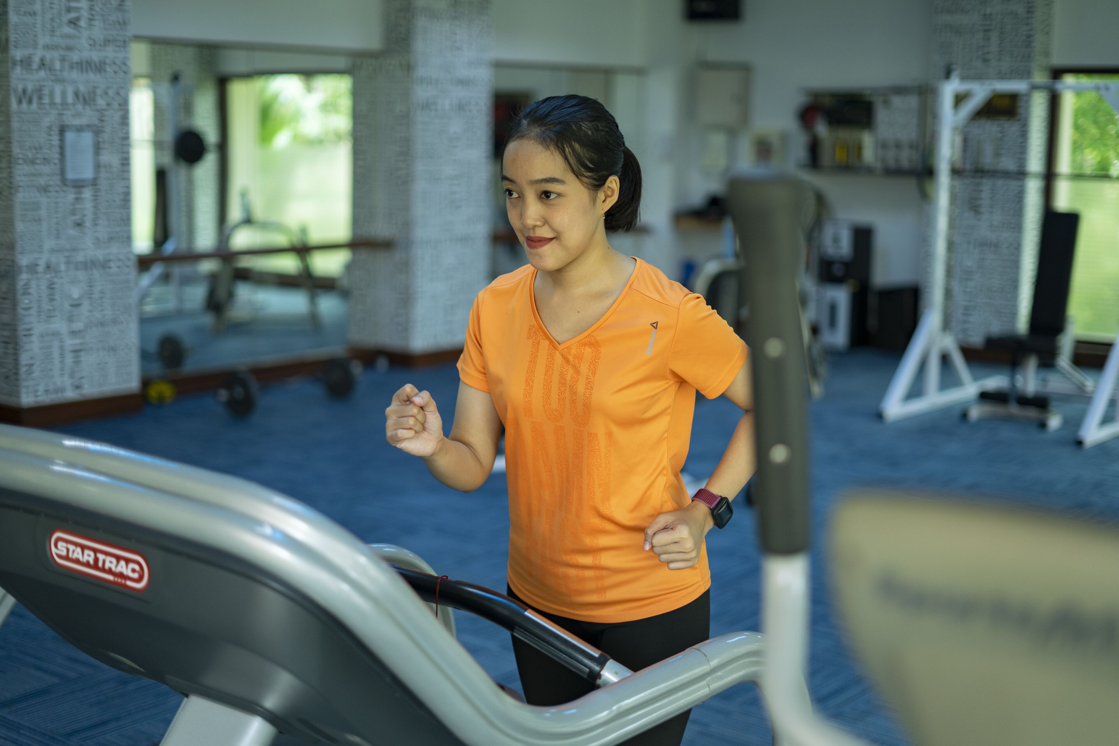 A person using a treadmill in a gym with visible weightlifting equipment and motivational posters on the walls.