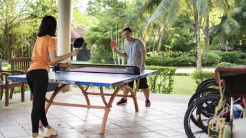 Mesa de ping pong instalada al aire libre donde una pareja juega, rodeada de bicicletas y follaje.