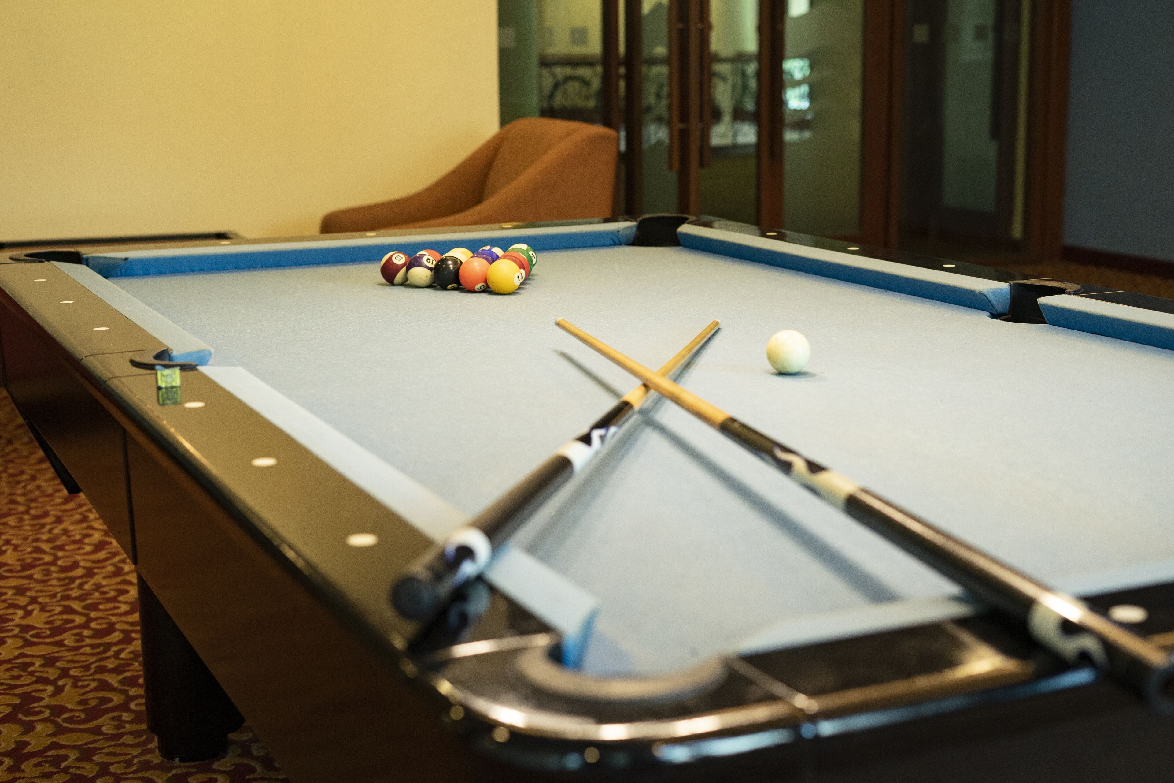 A pool table with balls and cues, a brown armchair, and a patterned carpet.