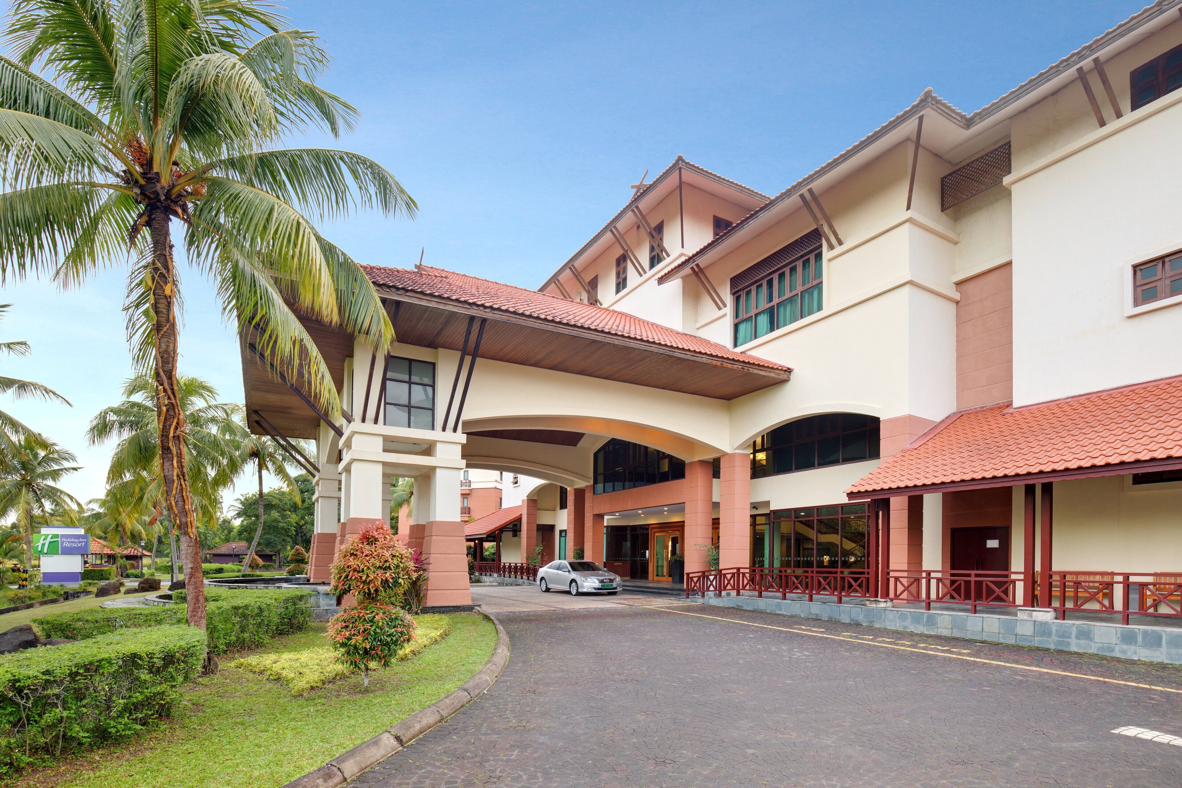 A hotel with a covered entrance, palm trees, and a car parked in front.