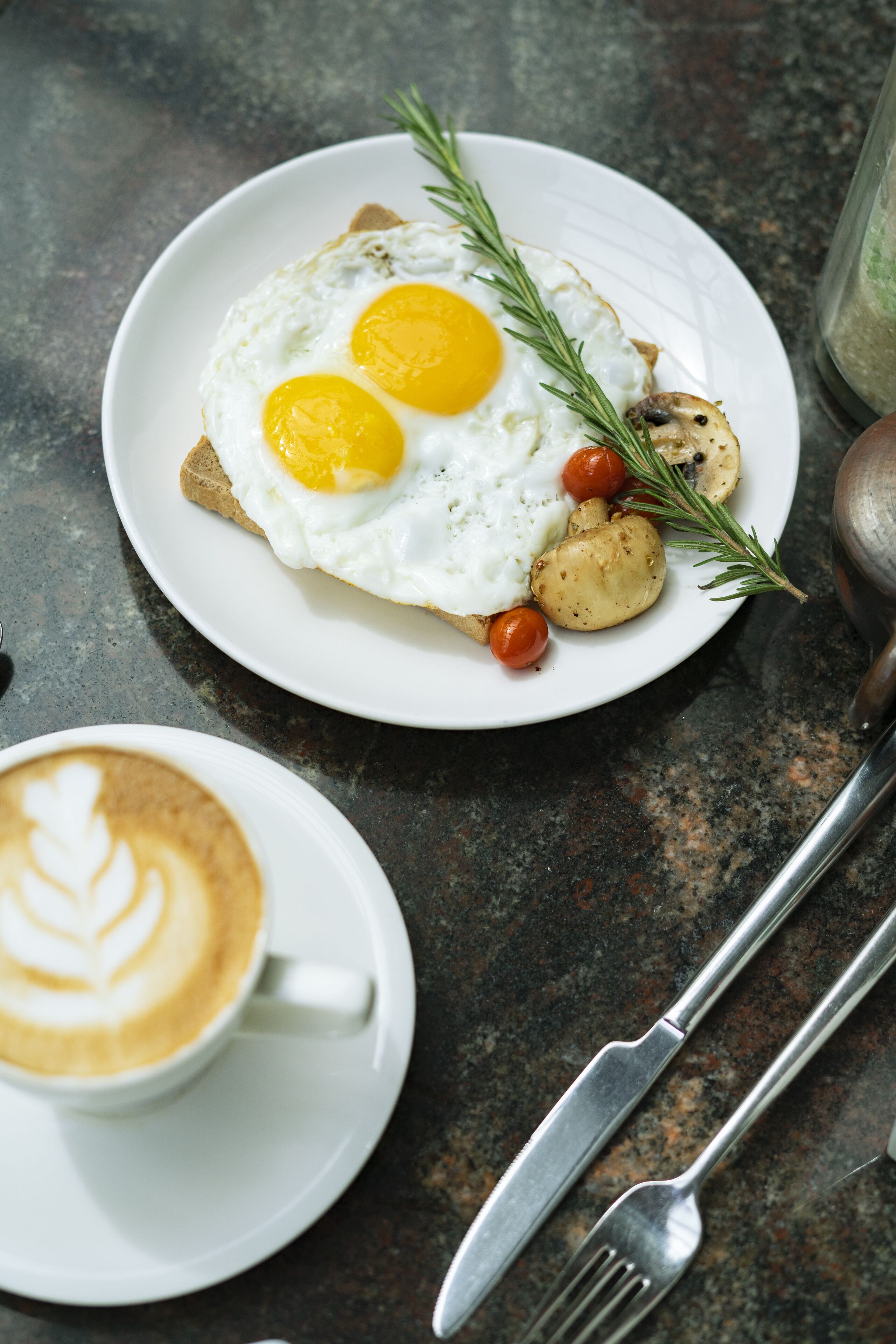 Un plato de desayuno con huevos, champiñones y una ramita de romero sobre un plato blanco.