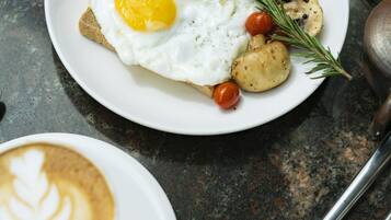 Un plato de desayuno con huevos, champiñones y una ramita de romero sobre un plato blanco.