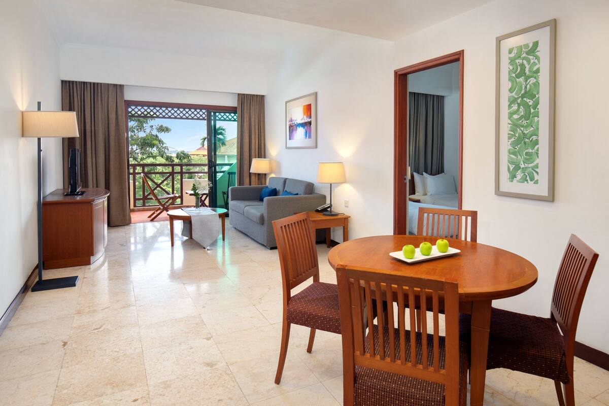 Habitación de hotel con comedor, sofá y balcón con vistas.