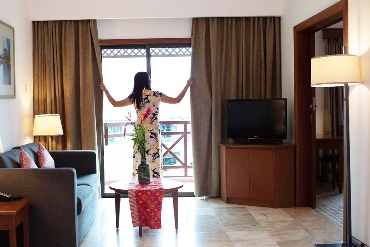 A hotel room with a sofa, a TV, a table with a vase, and curtains.