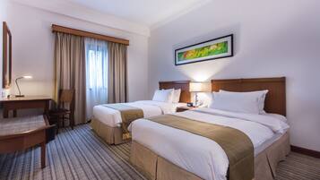 A hotel room with two beds, a desk, a chair, a window with curtains, a painting on the wall, and a carpeted floor.