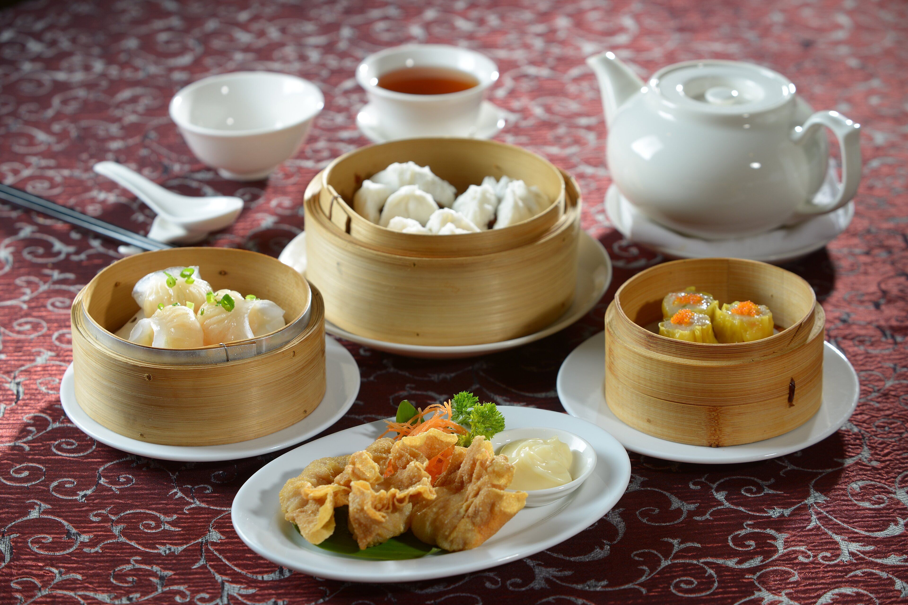 A table with various dishes, including dumplings and fried items, accompanied by bowls of soup and a teapot.