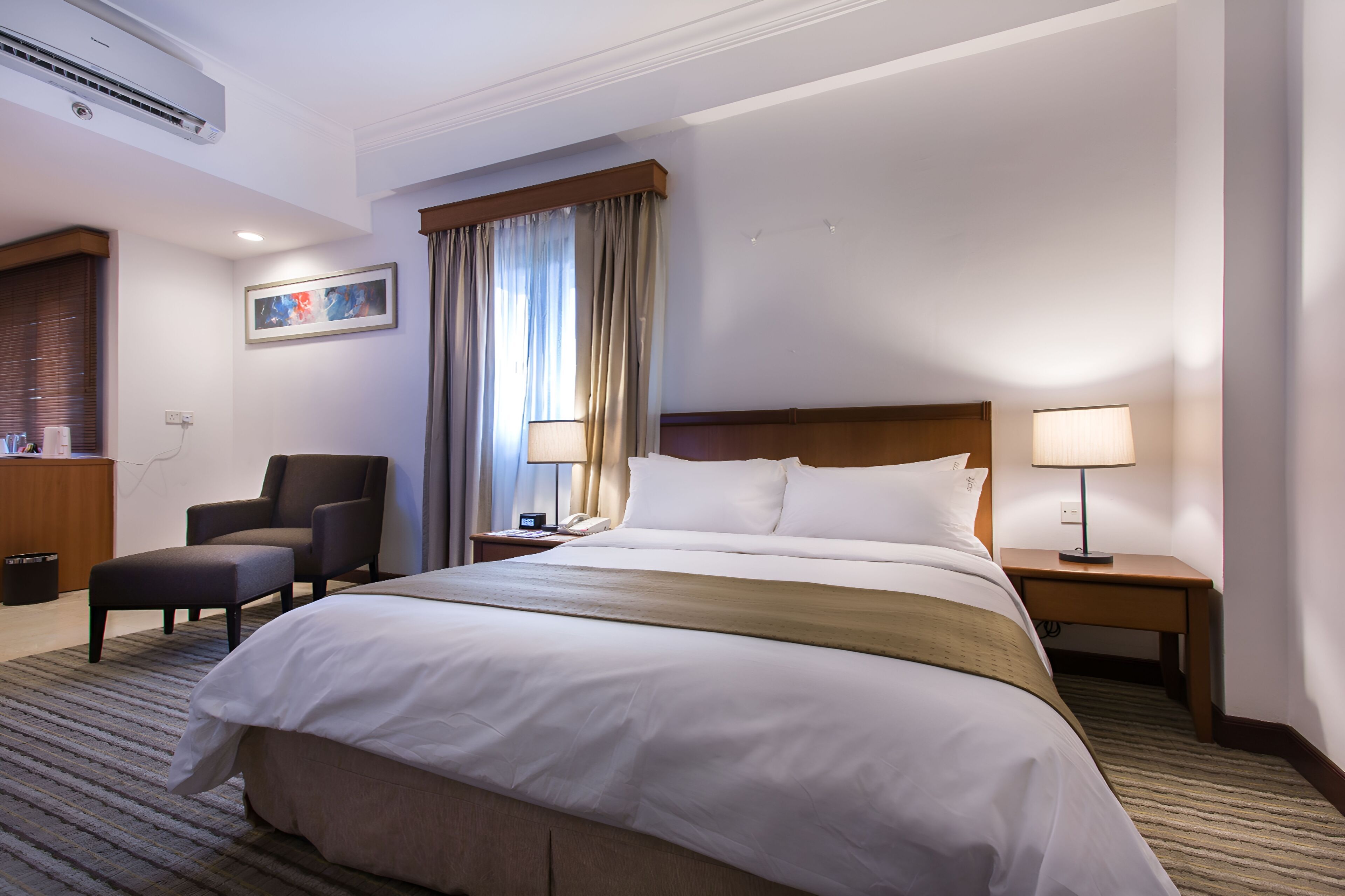 A hotel room with a large bed, two bedside tables with lamps, a chair, a desk, and a window with curtains.