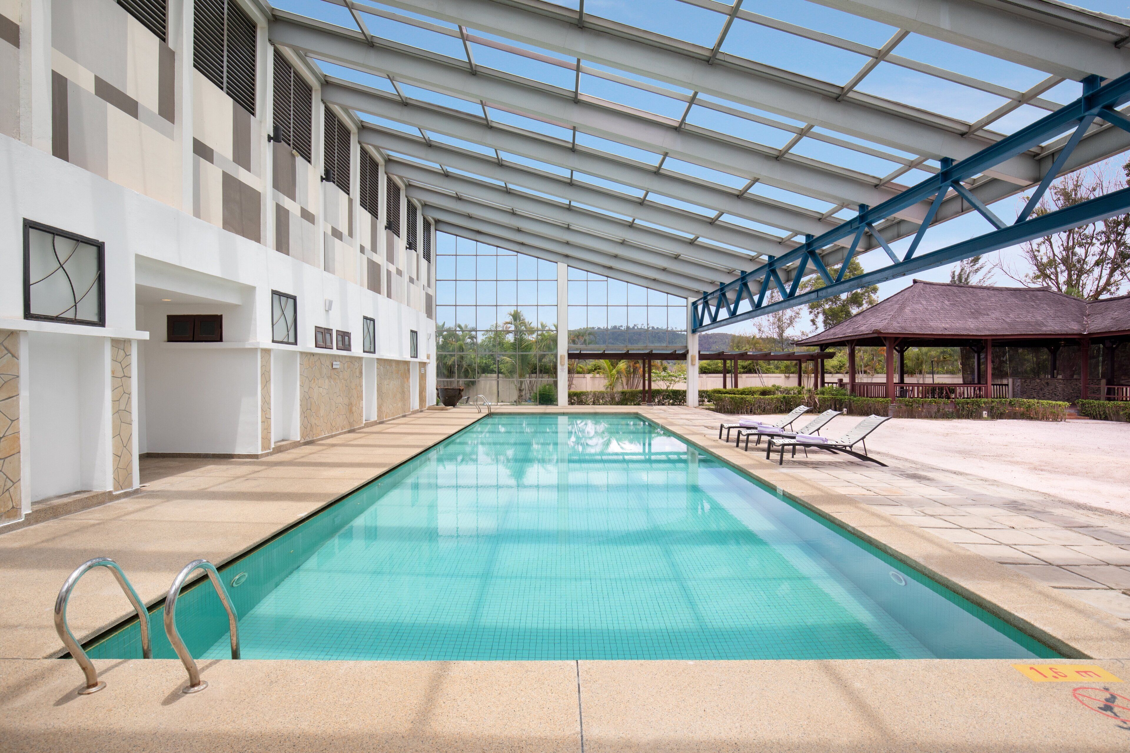 A swimming pool with a glass ceiling, lounge chairs, and a covered pavilion.
