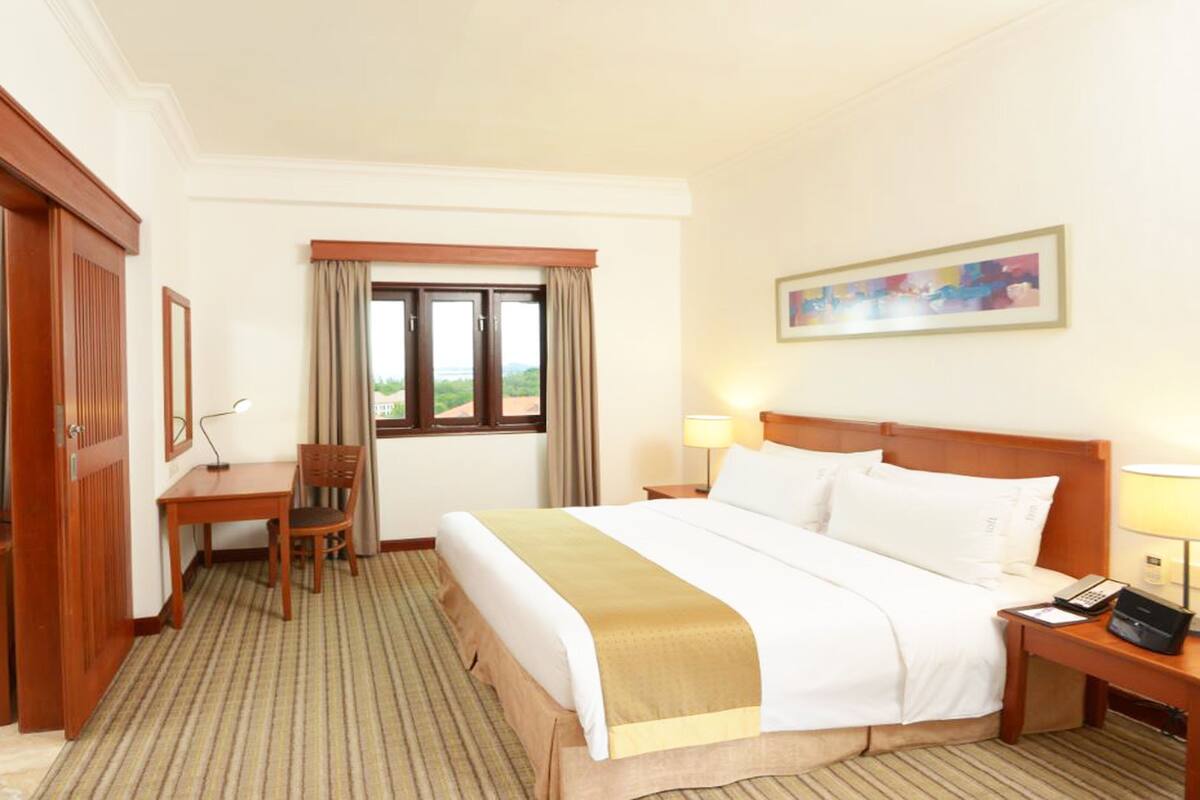 Una habitación de hotel con cama, escritorio, silla, televisor y ventana con cortinas.