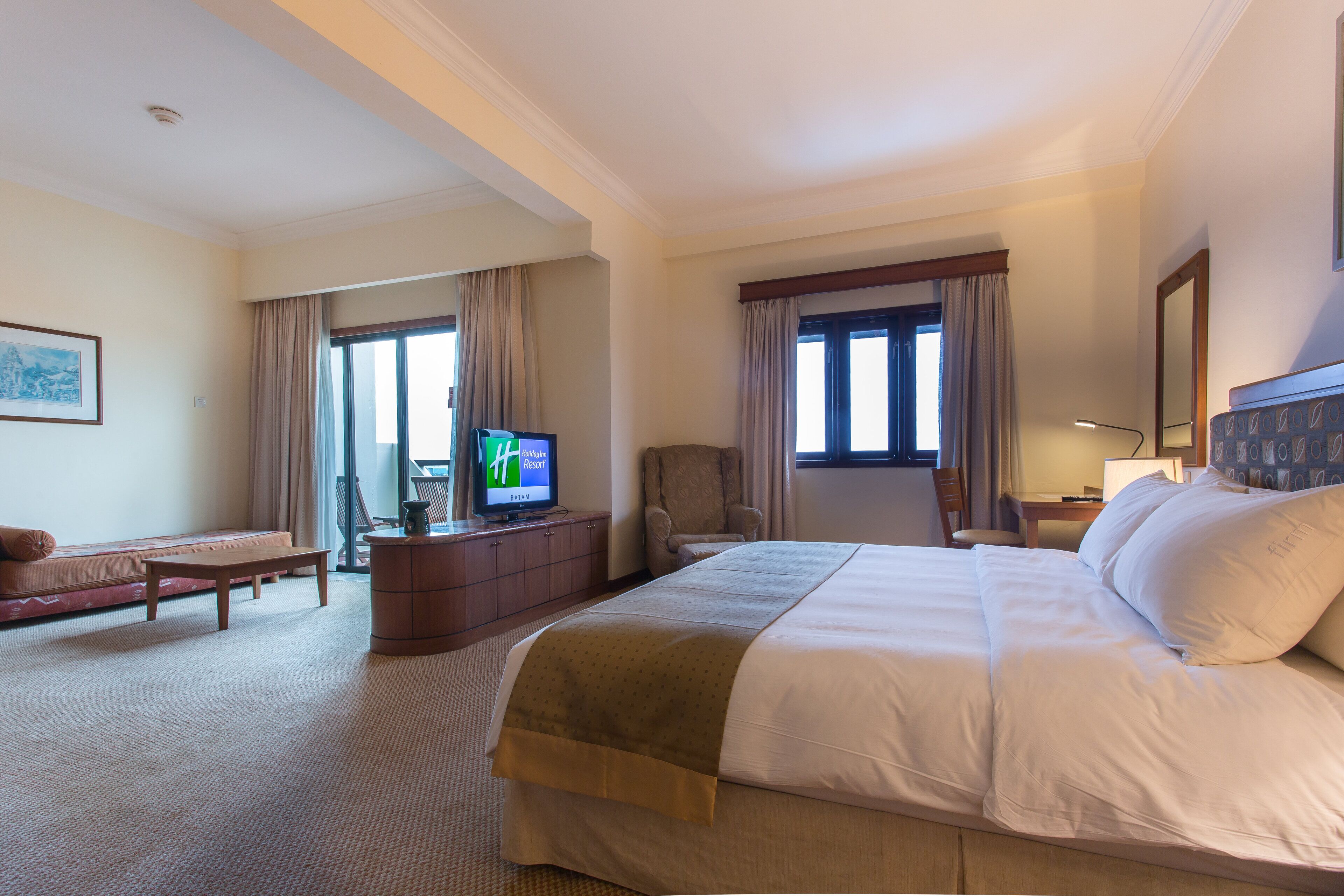 A hotel room with a large bed, a desk, a chair, a television, and a window with curtains.