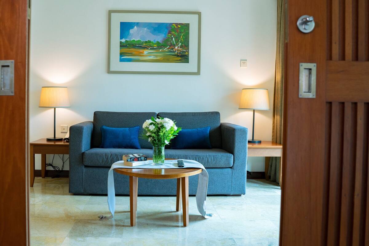 Una habitación con un sofá gris, dos lámparas, un florero con flores y un cuadro en la pared.