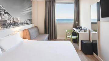 Ein Hotelzimmer mit einem Bett, einem Schreibtisch, einem Sessel, einer Couch, einem großen Fenster mit Vorhängen und einem Stadtbild-Wandgemälde.