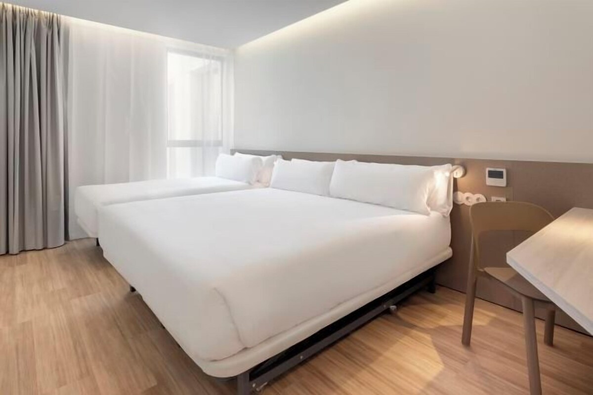 A modern hotel room with a large bed, a bedside table, and a chair.
