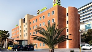 Ein Hotel mit moderner Backsteinfassade, mehreren Balkonen und einem Parkplatz mit einigen Autos.